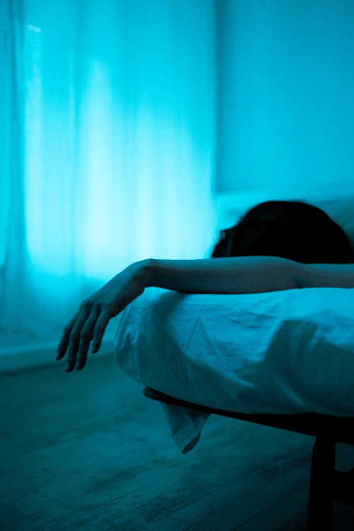 Person lying down in a dimly lit room, representing mental health struggles and the impact of delaying care.