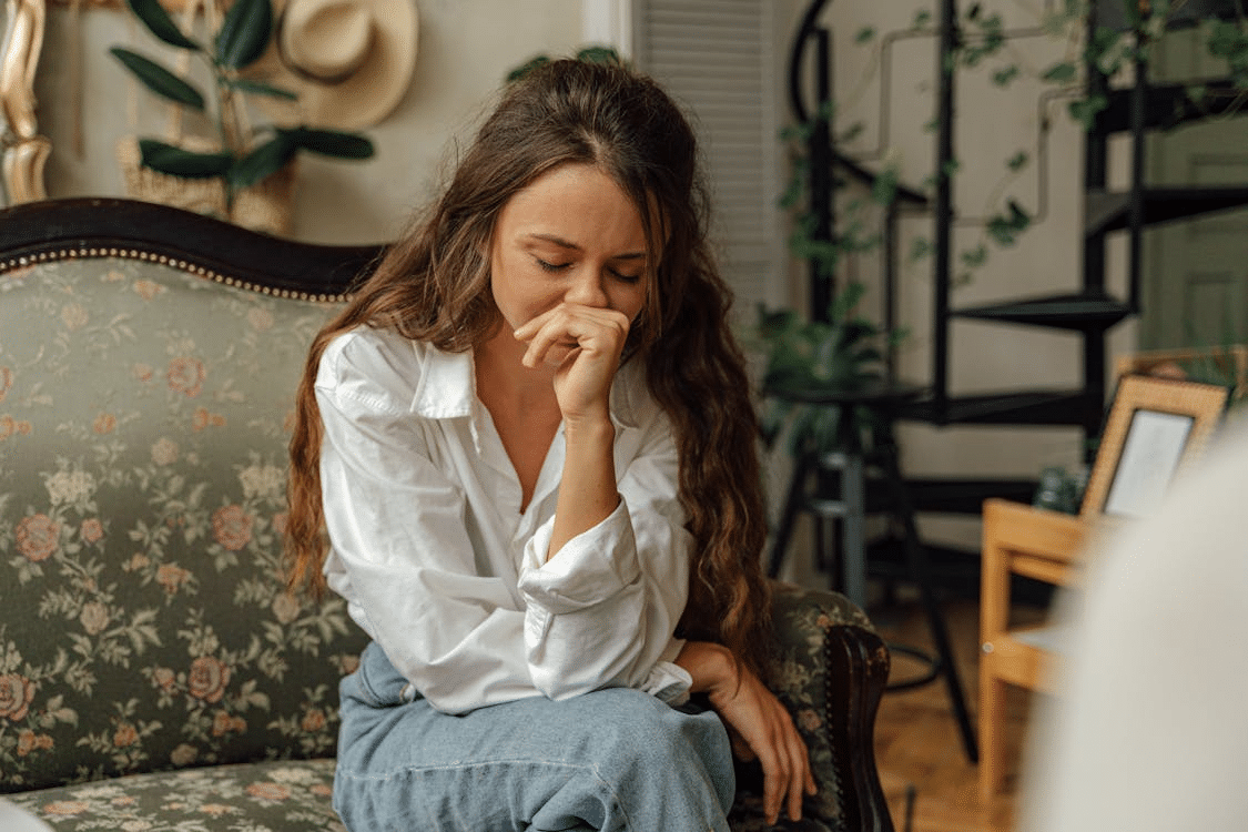 Woman in a white dress shirt and blue jeans sitting on a floral sofa.