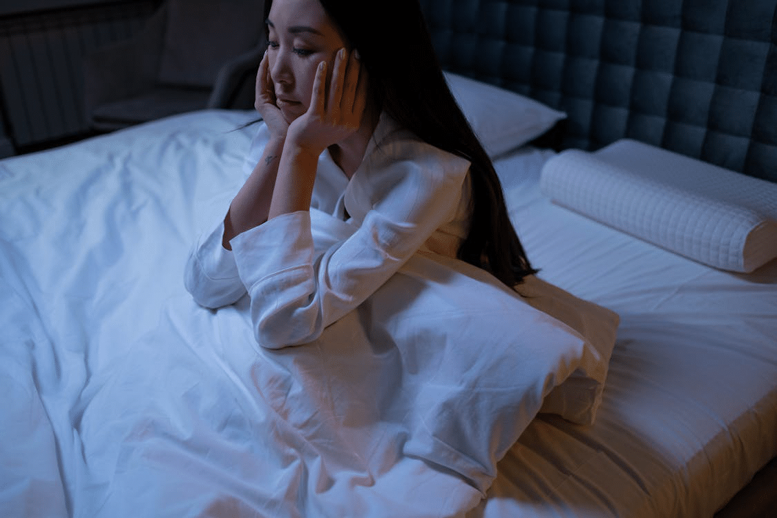 Woman sitting on bed appearing restless due to insomnia, symbolizing the mental health effects of chronic sleep loss.
